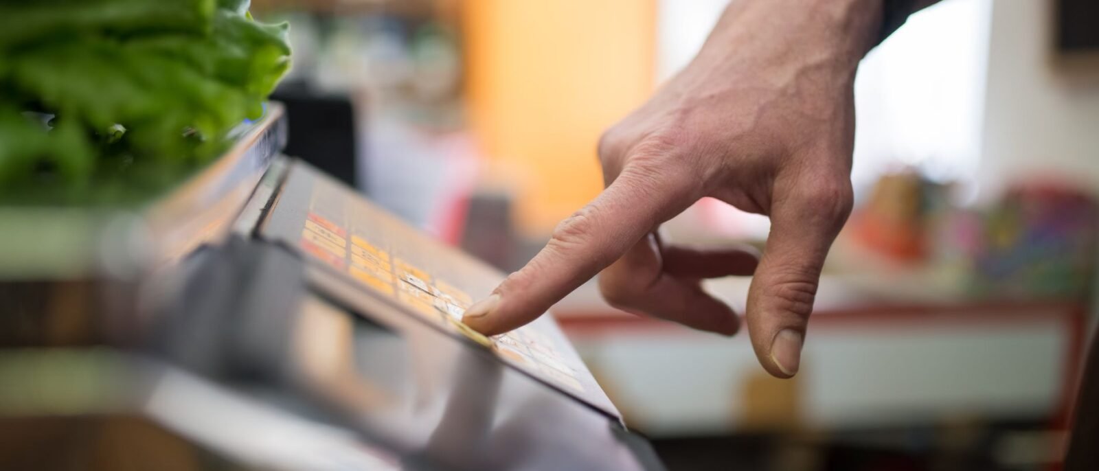 Uma mão interagindo com uma balança digital em uma seção de produtos, enfatizando tecnologia nas compras