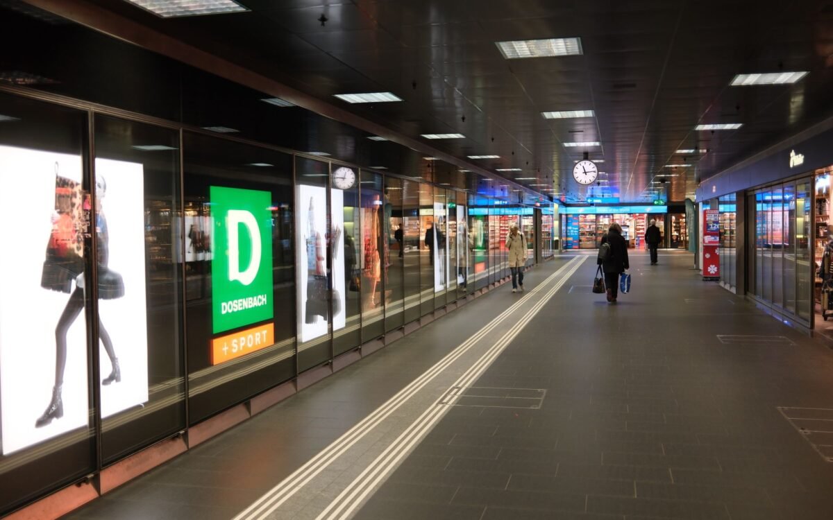 Visão ampla de um corredor de shopping movimentado com pessoas, lojas e um relógio em destaque