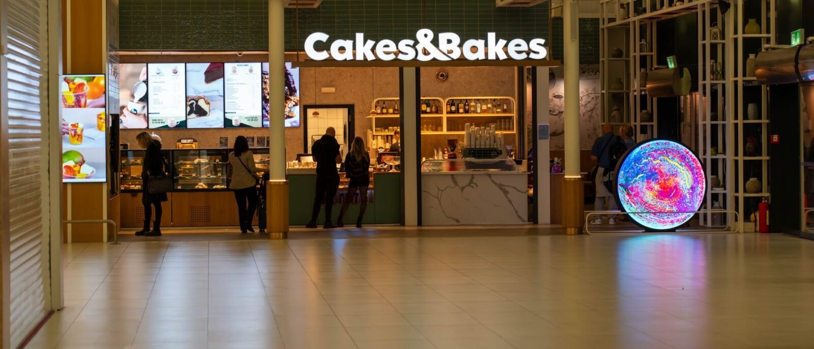 Uma padaria moderna, Cakes & Bakes, em um shopping de Zagreb à noite com compradores por perto