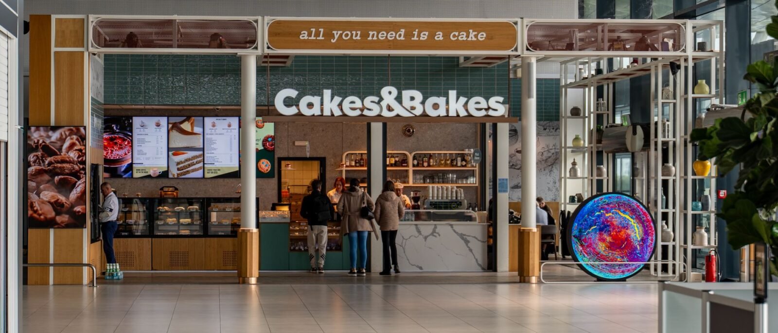 Vista interna da padaria Cakes & Bakes no Aeroporto de Zagreb com clientes e design contemporâneo
