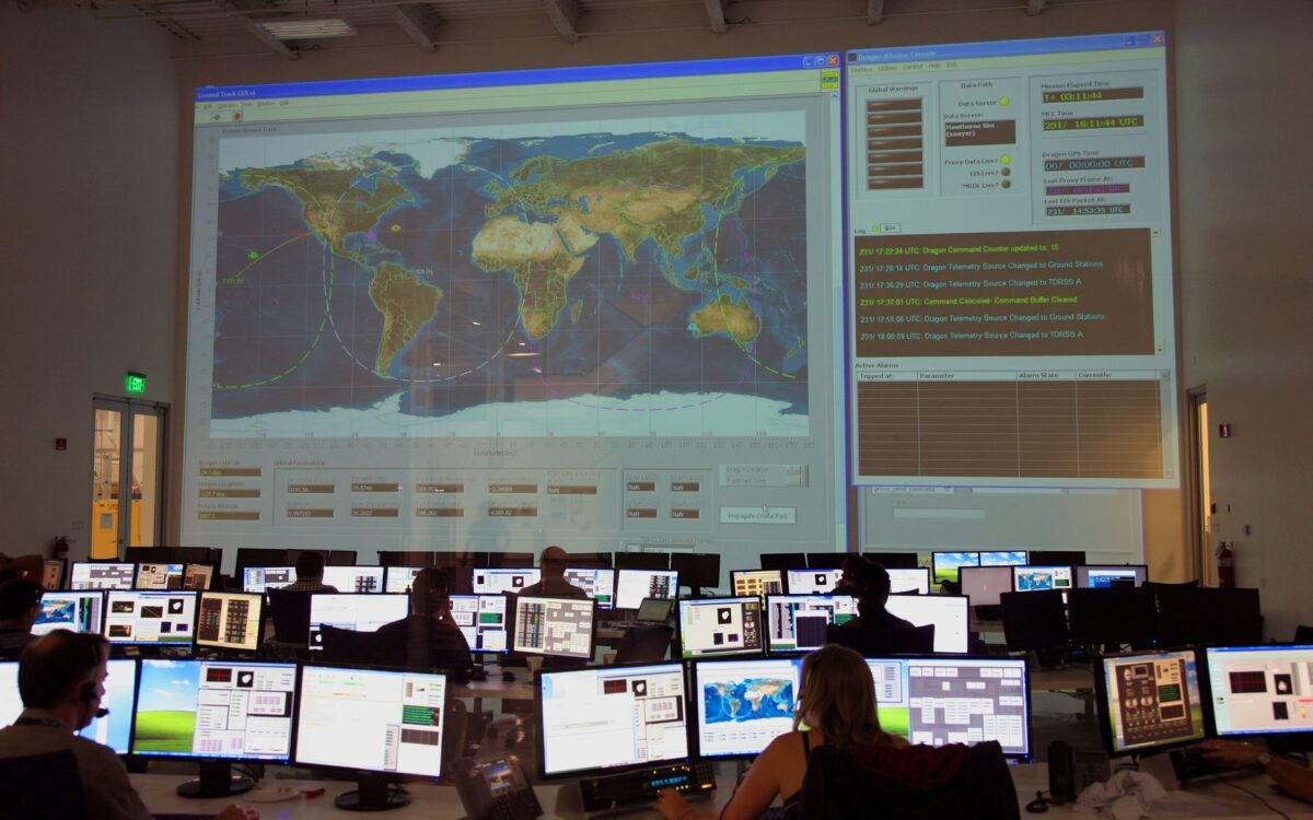Vista traseira de funcionários irreconhecíveis trabalhando em computadores em sala de controle de voo com grande mapa interat